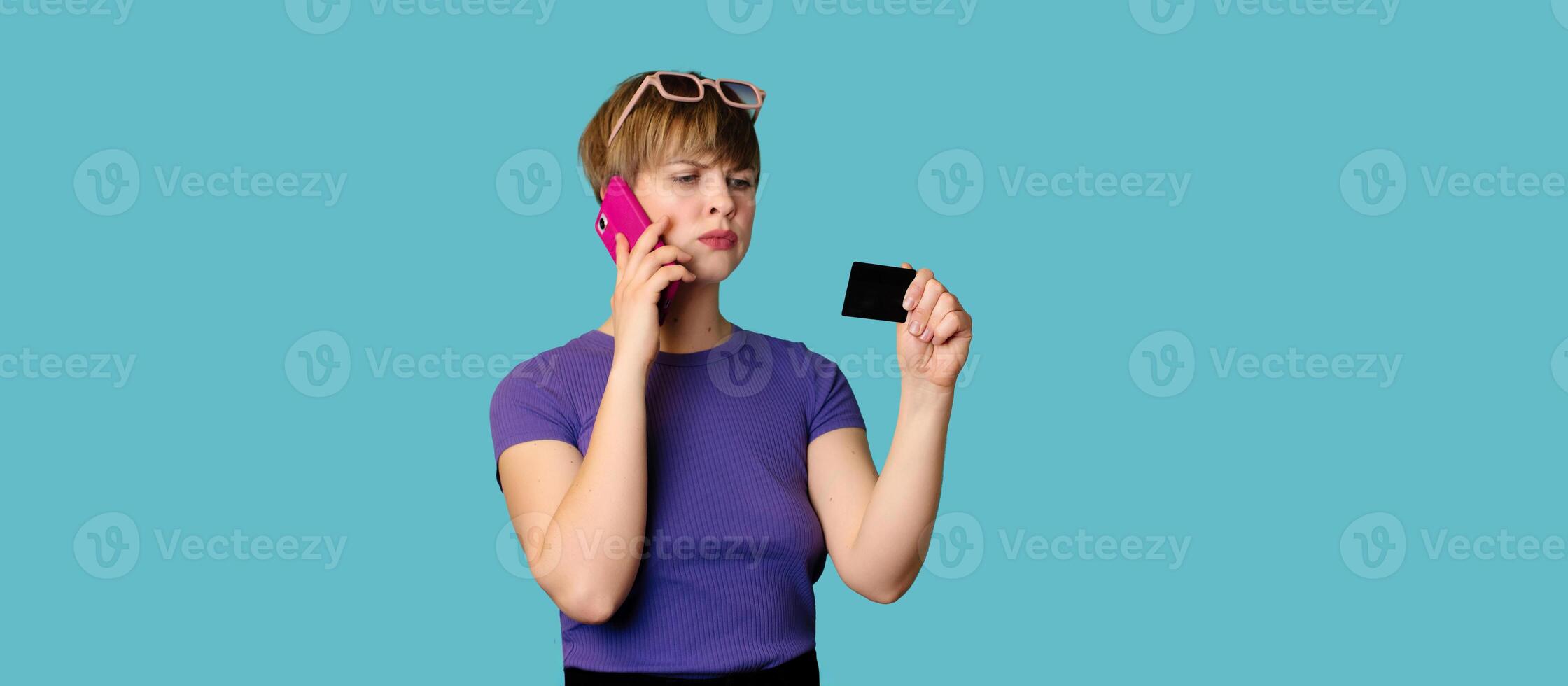 An incredulous pretty modern girl advertises, makes online purchases, holds a credit card in her hands and talks on a smartphone. Panoramic image photo