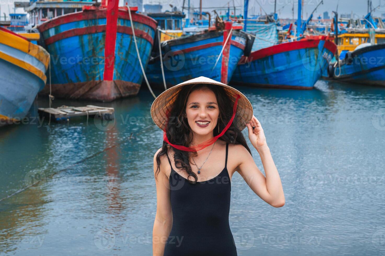 A female traveler wearing a traditional Vietnamese hat inspects traditional wooden boats at the port of Da Nang. photo