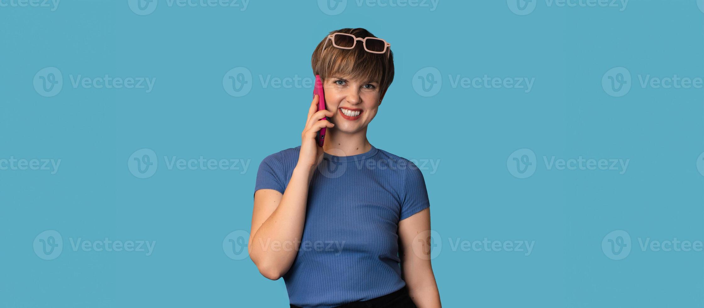 A Caucasian young woman is talking emotionally on a mobile phone on a blue background. Panoramic banner. A place for your text. Technology concept photo