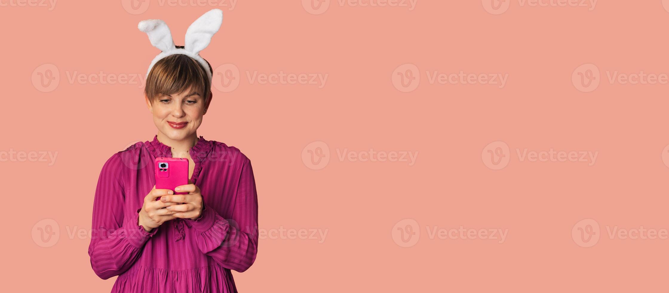 A beautiful girl with bunny ears on a colored background with a smartphone in her hands. photo