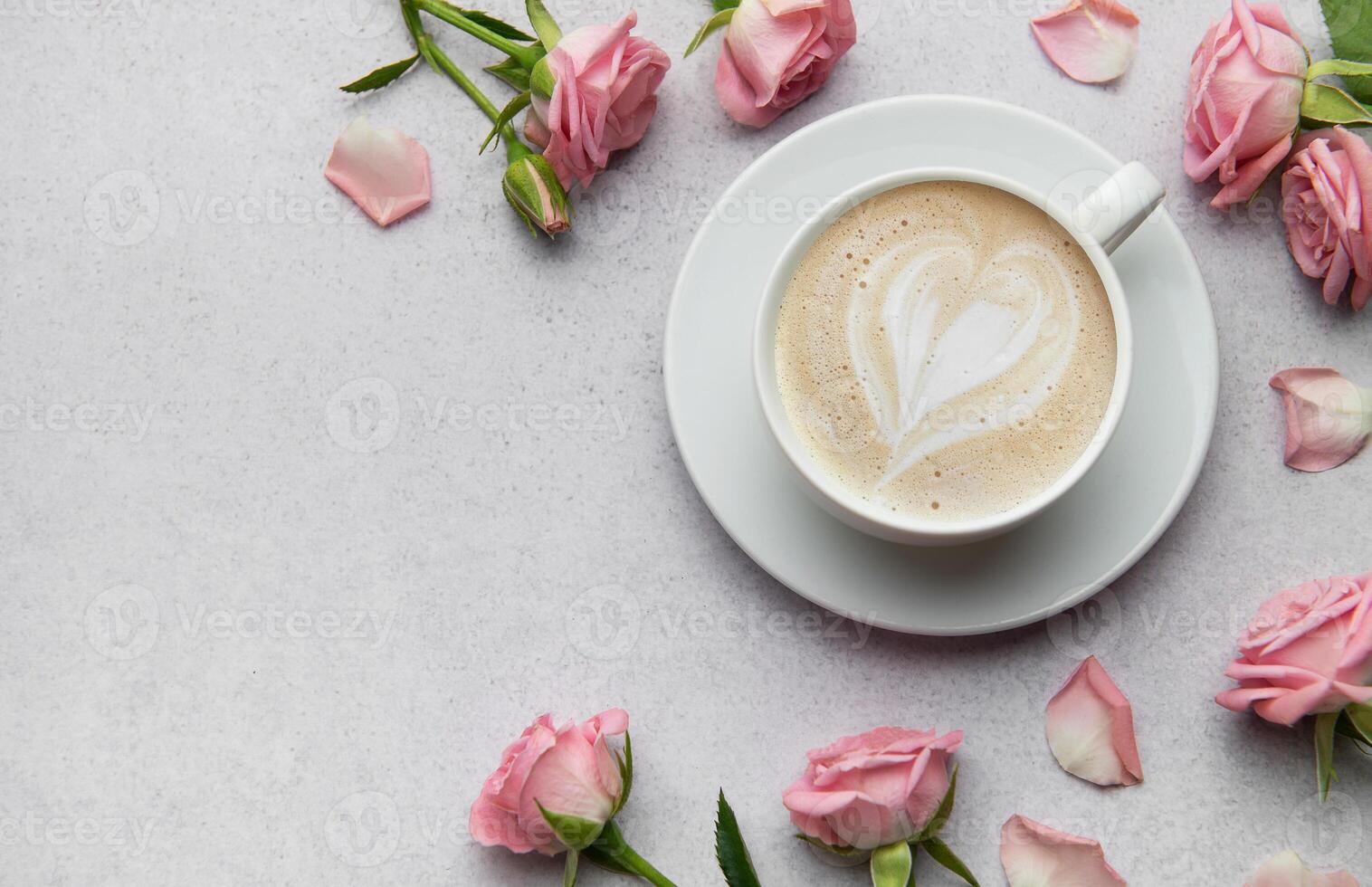 Cup of cappuccino with latte art heart and pink roses on grey background photo