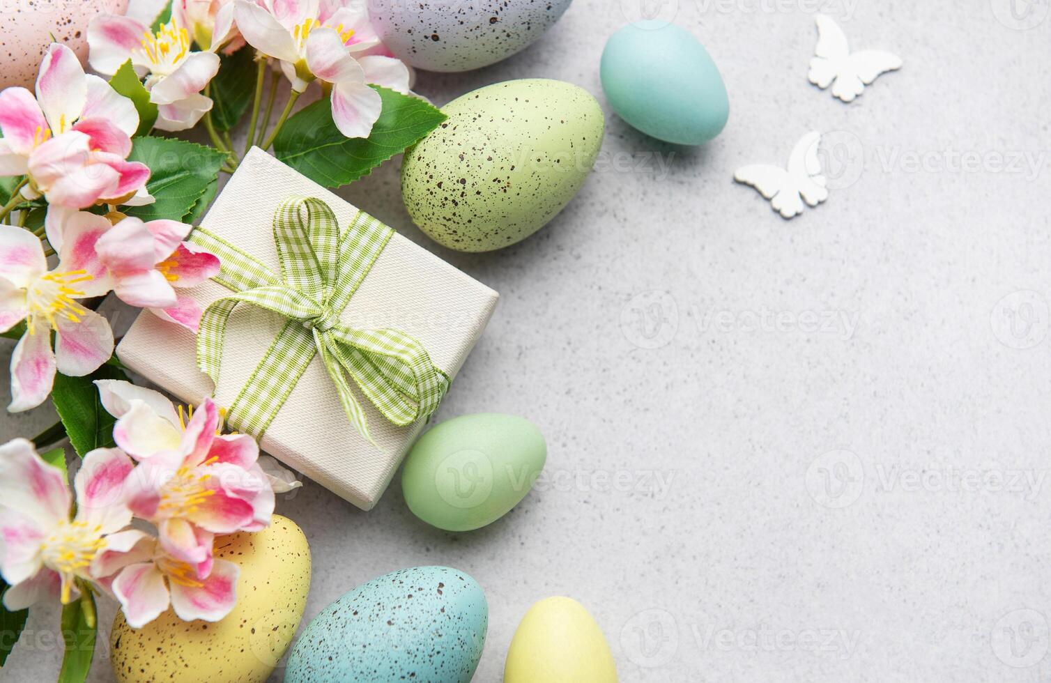 Easter eggs, gift box and spring flowers creating a festive border on grey background photo