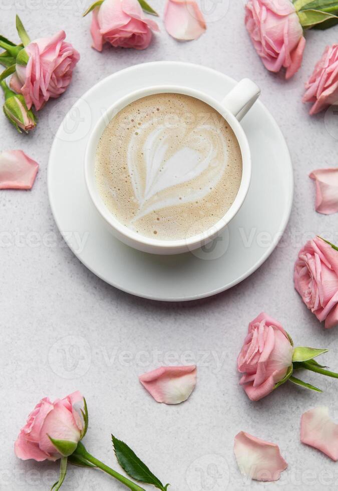 Cup of coffee with latte art heart and pink roses on grey background photo