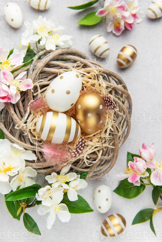 Easter eggs are lying in a nest with spring flowers on a gray background photo