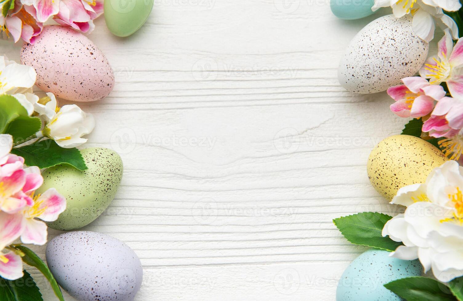Colorful easter eggs and spring flowers creating a frame on white wood photo