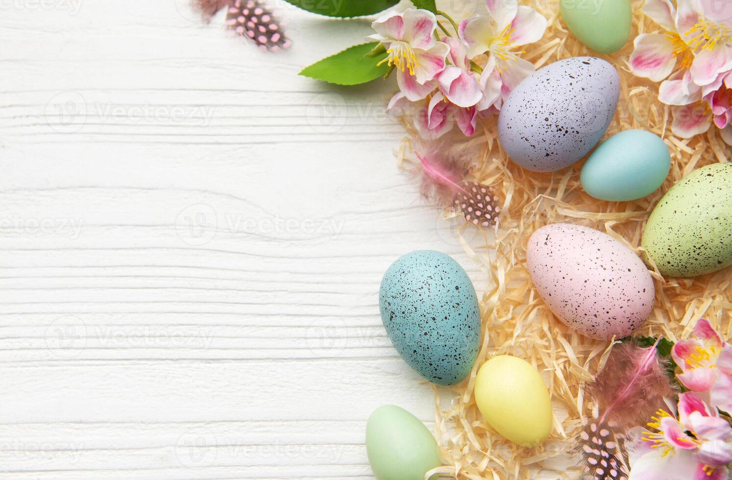 Easter eggs and spring flowers creating a frame on white wooden background photo