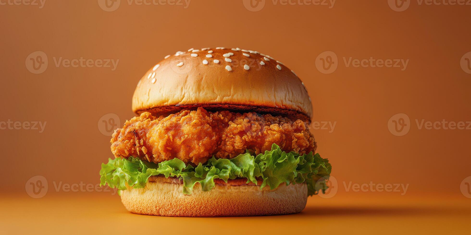 Crispy fried chicken sandwich with fresh lettuce and sesame seed bun on a warm orange background photo