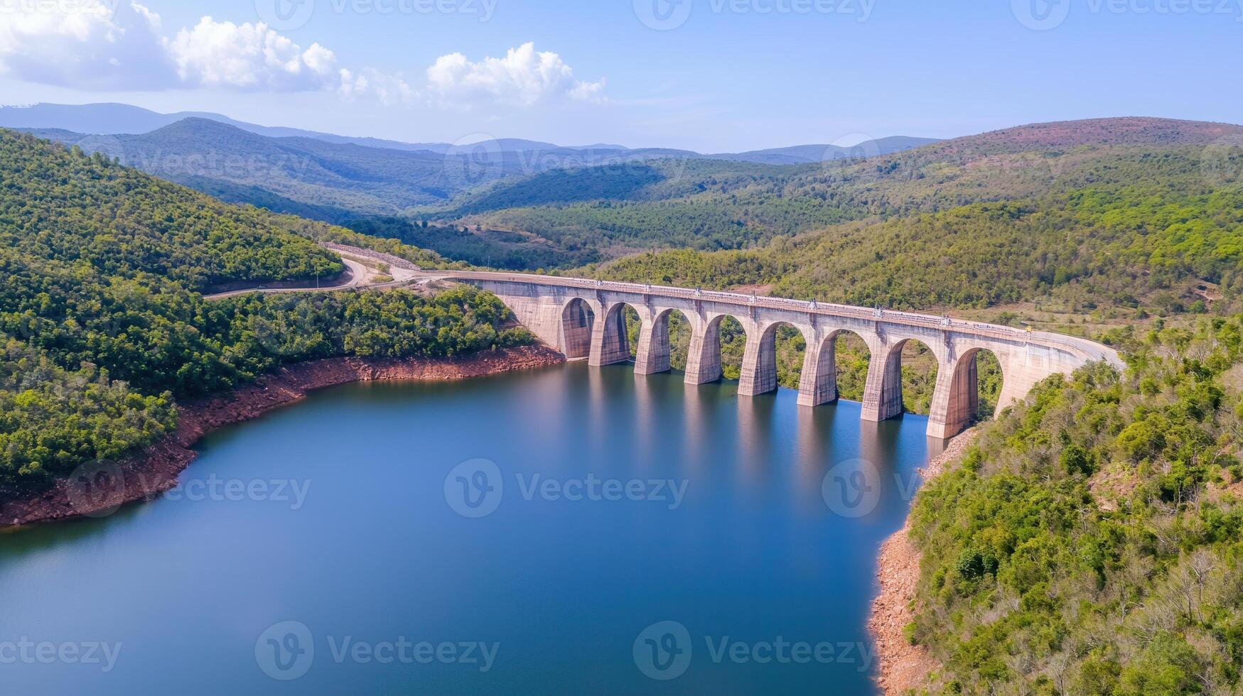 stunning hydroelectric dam spans serene lake, surrounded by lush green hills and mountains. clear blue sky enhances tranquil atmosphere photo