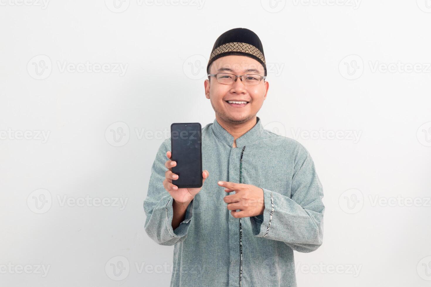 CheerfulAsian Muslim man wearing white clothes pointing phone pose, Ramadan Eid Al Fitr and eid adha days celebration isolated white background. Islamic celebration concept. photo