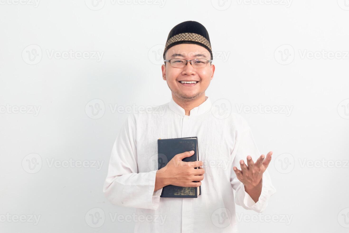 Asian Muslim man wearing white clothes welcoming and holding quran during Ramadan Eid Al Fitr and eid adha days celebration on white background. Islamic celebration concept. photo