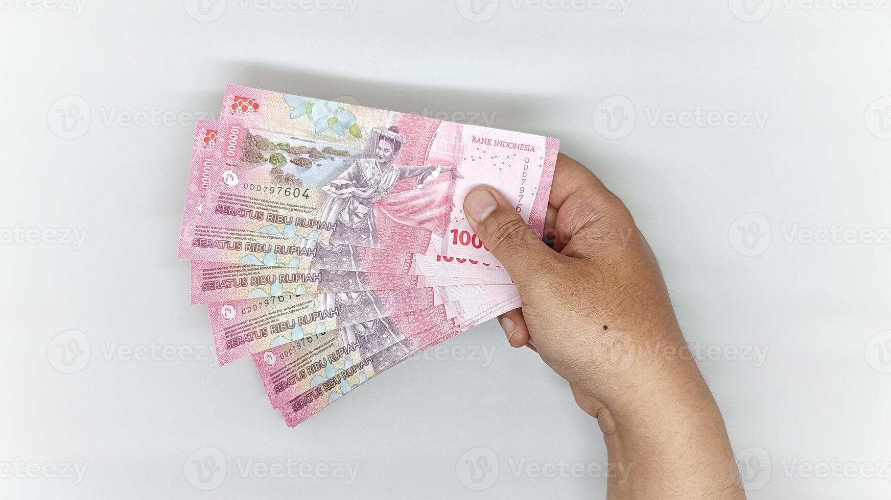 one hand holding stack of Indonesian banknotes in the 100000 rupiah denomination photo