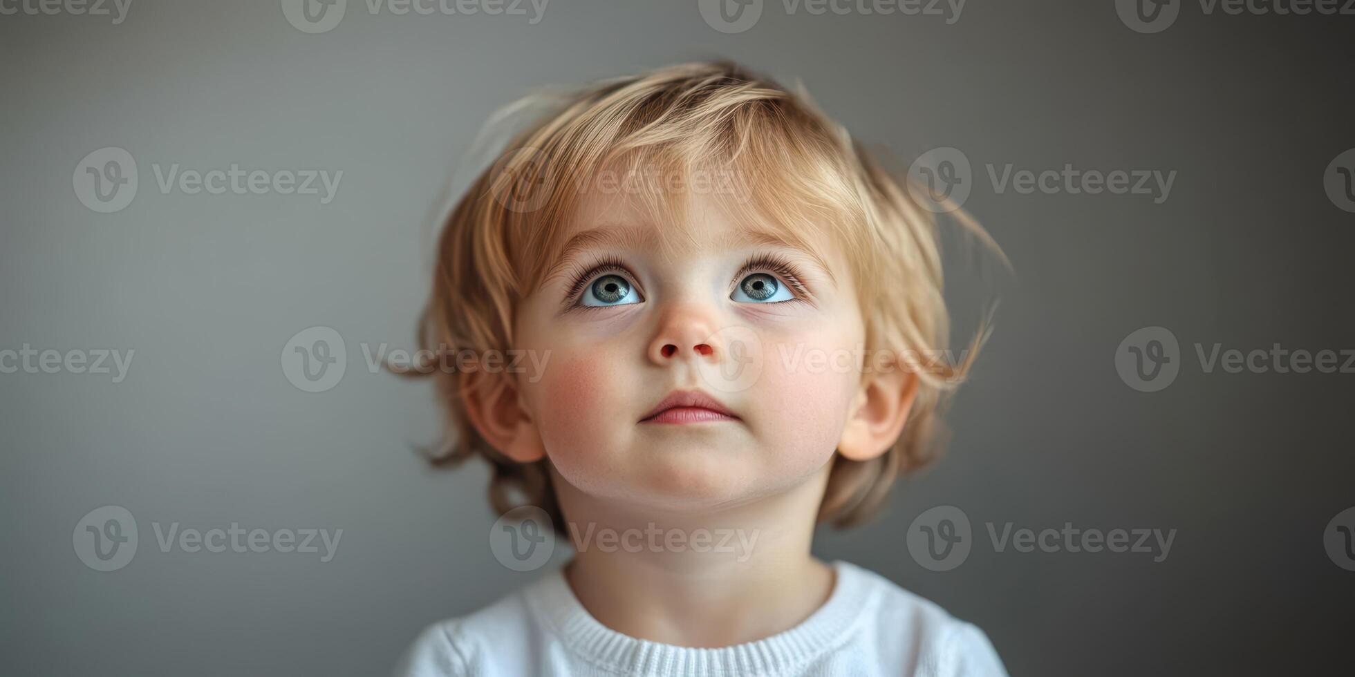 Child gazing up with curiosity while seated against a plain background in soft natural light photo