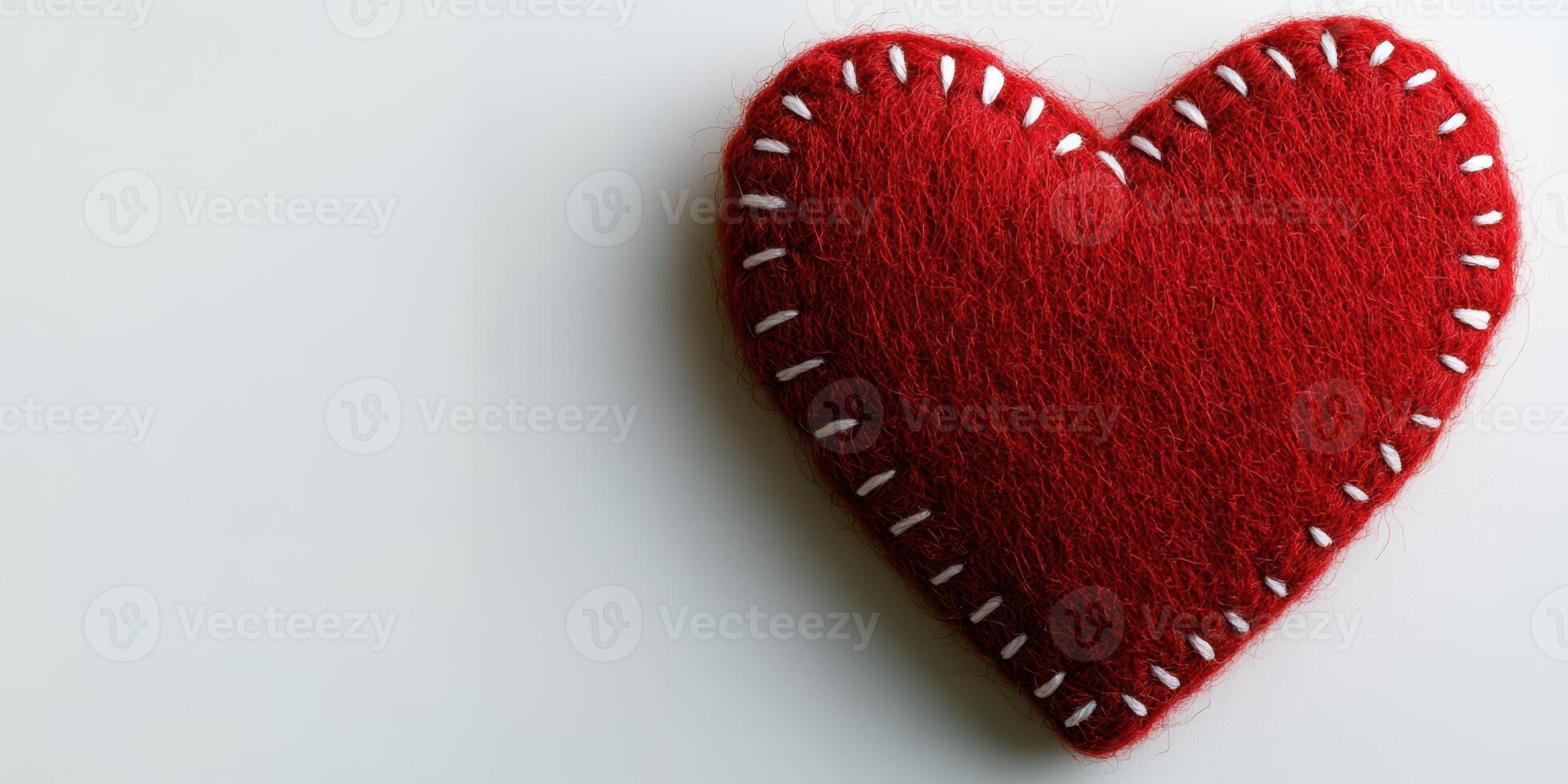 Handmade red felt heart with white stitching resting on a plain background during daylight photo