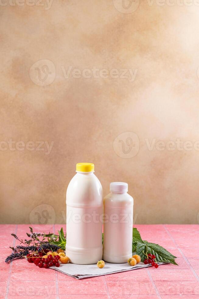 Two white bottles of kefir or yogurt with berries and herbs on pink table photo