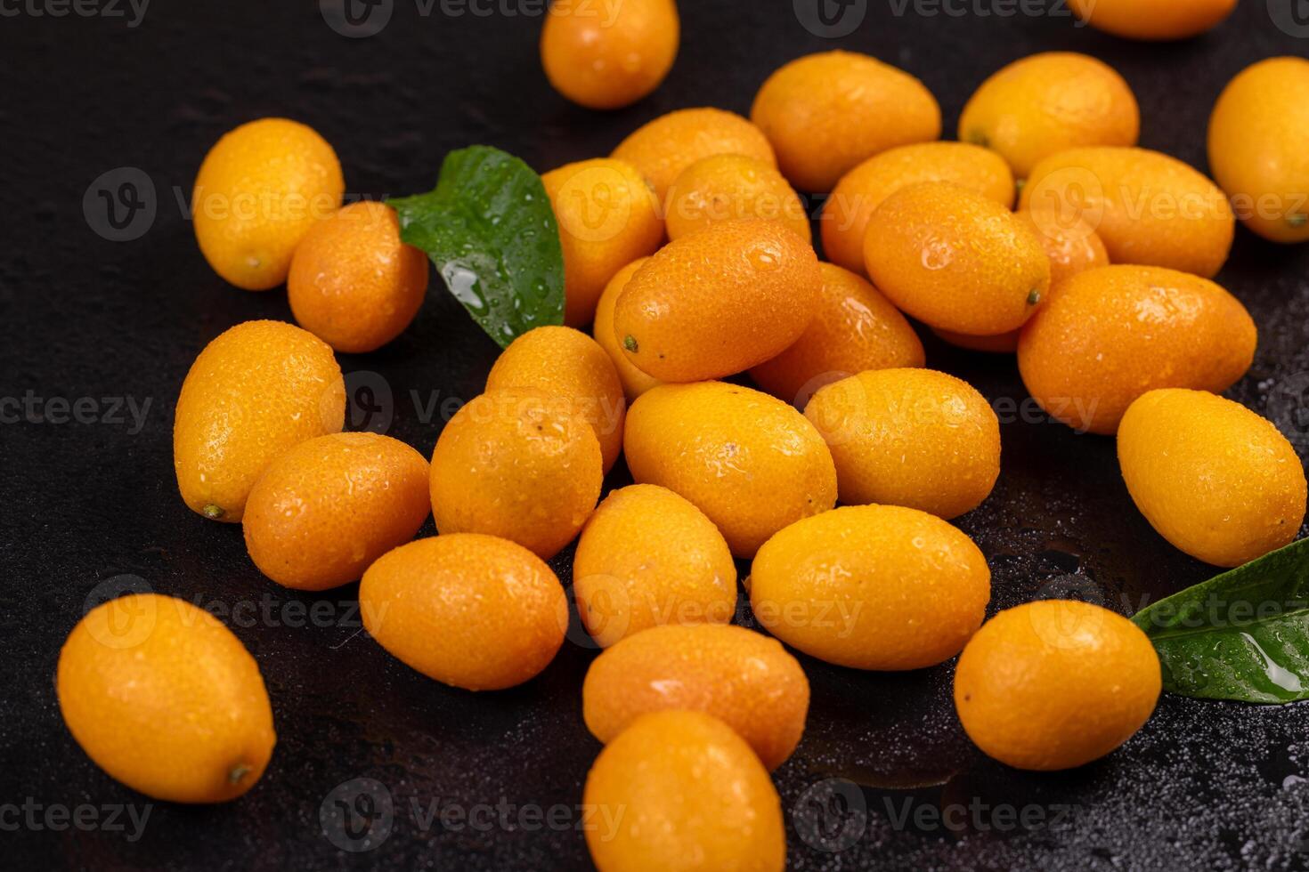 Vibrant kumquats, adorned with water droplets and accompanied by green leaves, create a visually appealing display on a dark surface photo
