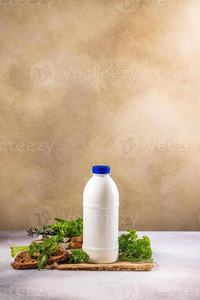 White bottle of milk or yogurt with blue cap, slices of bread and herbs on rustic background photo