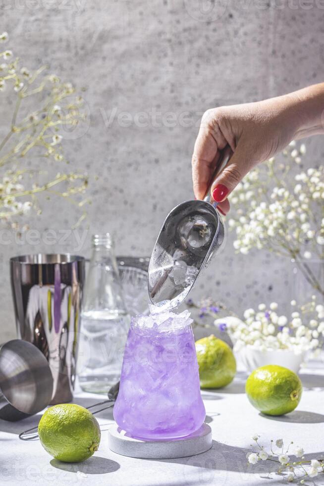 Bartender adding ice to purple cocktail with lime and shaker photo