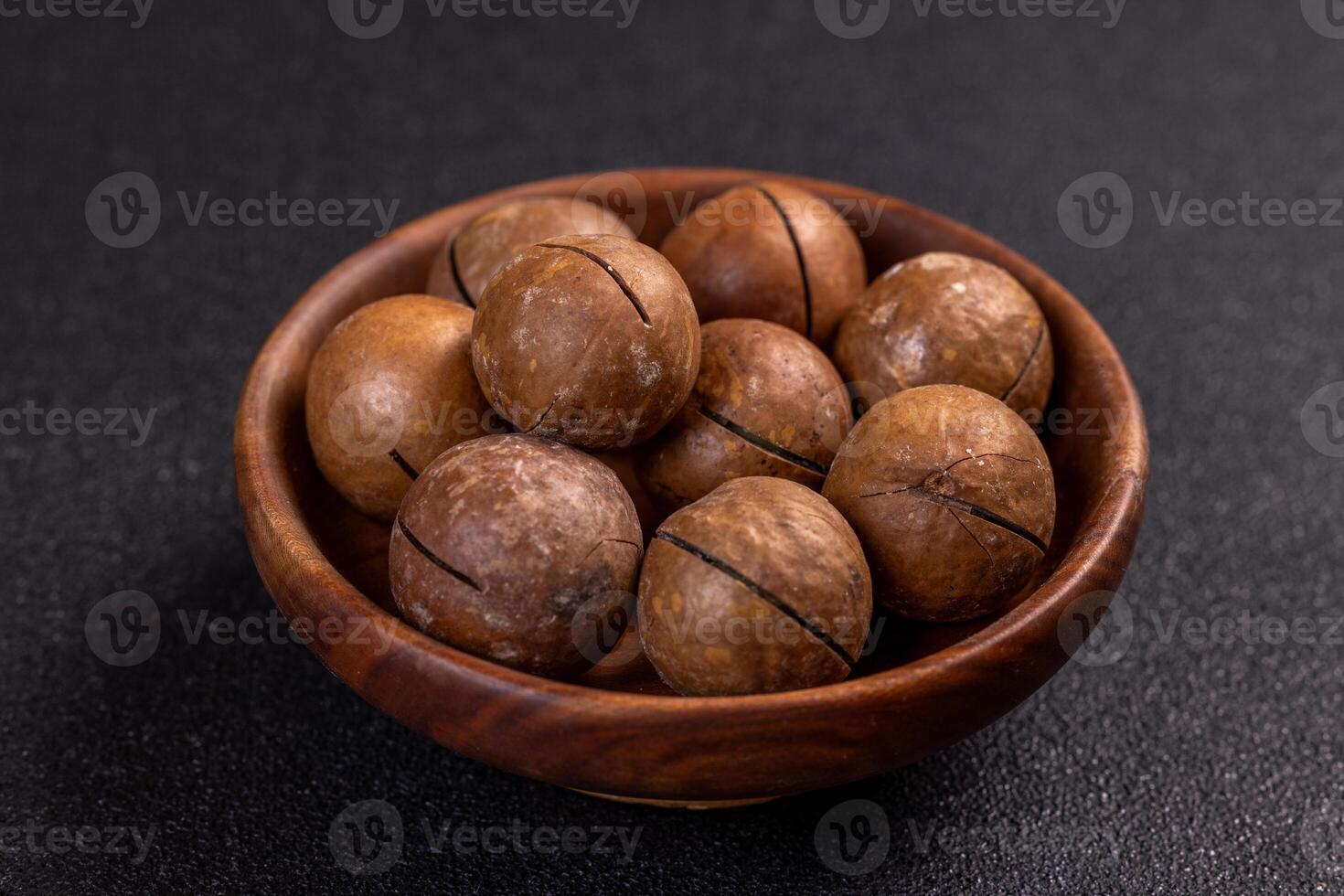 Macadamia nuts piled in wooden bowl on dark background photo