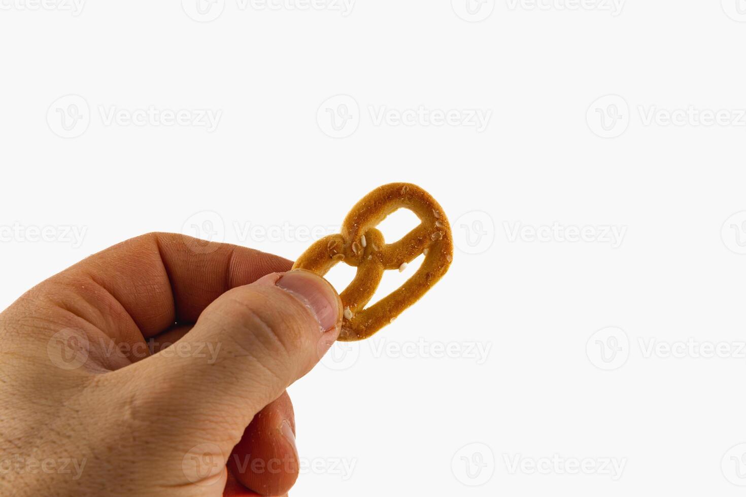 Hand holding a small pretzel against a bright background in a kitchen photo