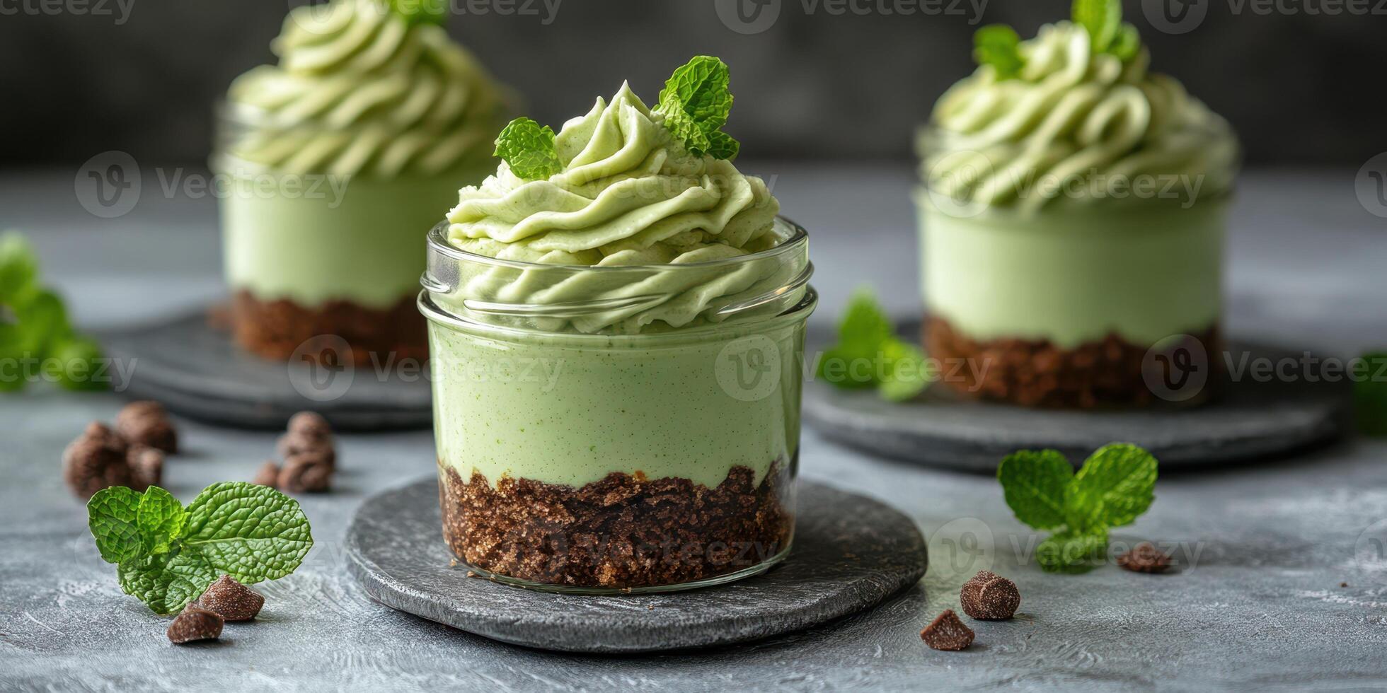 Delicious matcha mousse topped with mint leaves served in elegant glass jars on a slate background photo