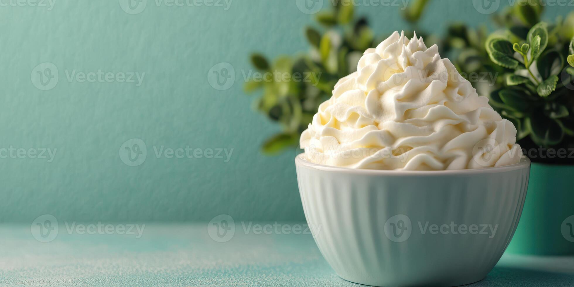 Delicious whipped cream topping served in a bowl against a calming teal background with greenery photo