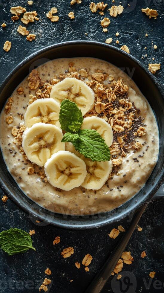 Creamy oatmeal bowl topped with banana slices and mint leaves served with granola and chia seeds photo