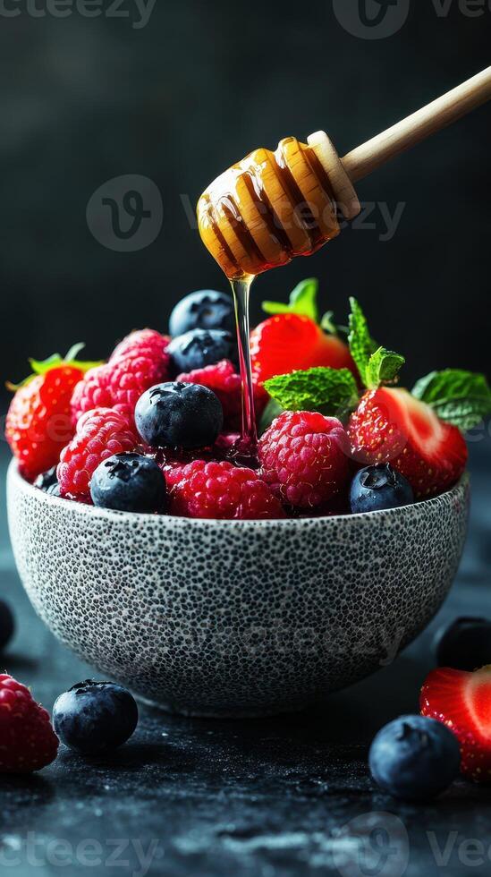 Fresh berries drizzled with honey in a textured bowl on a dark surface photo