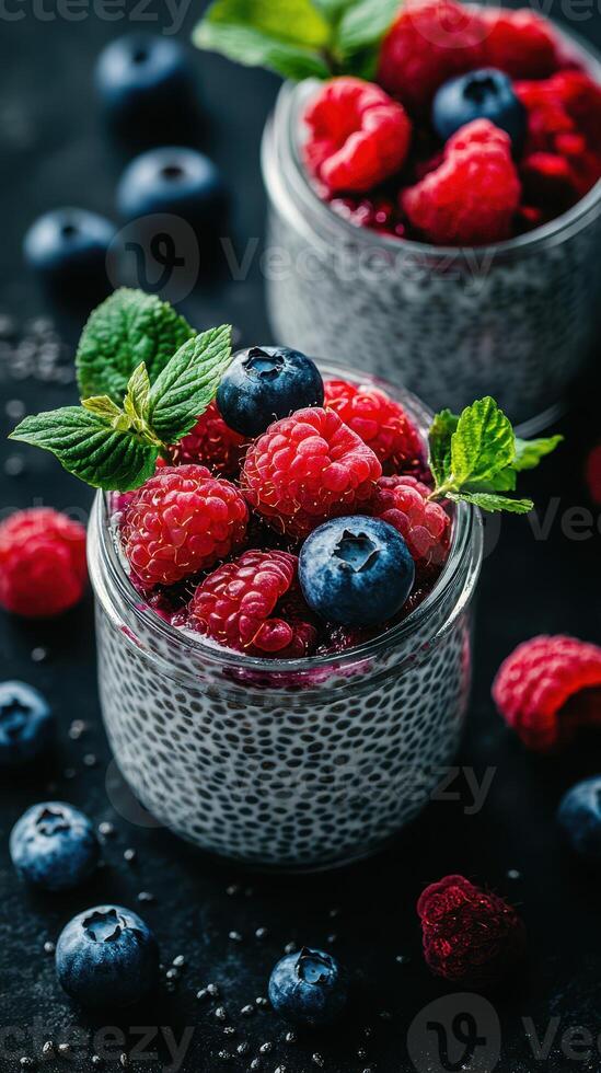 Chia pudding topped with fresh raspberries and blueberries in glass jars on a dark surface photo