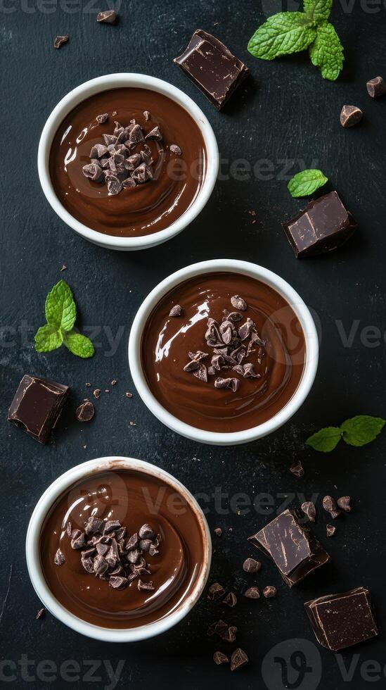 Delicious chocolate mousse served in white bowls with mint leaves and chocolate chunks on a dark stone background photo