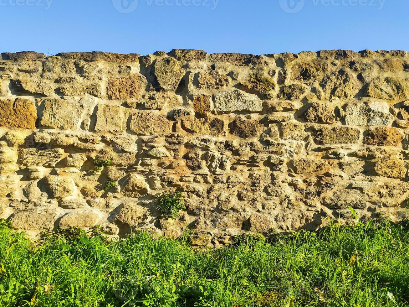 Rustic stone wall texture. Ancient, weathered masonry under a clear sky. Ideal for backgrounds, architectural designs, or historical projects. Evokes a sense of age and durability. photo