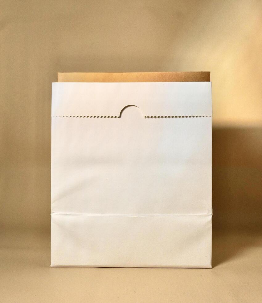 Empty white and brown paper bag container isolated on vertical brown cream background. photo