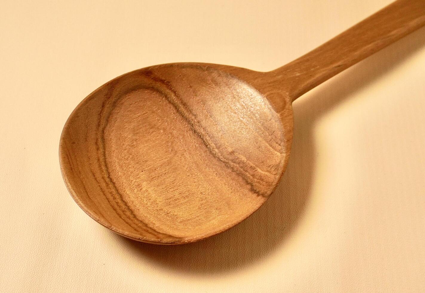 Close up brown wooden spoon kitchen utensil isolated on horizontal yellow cream colored background. photo