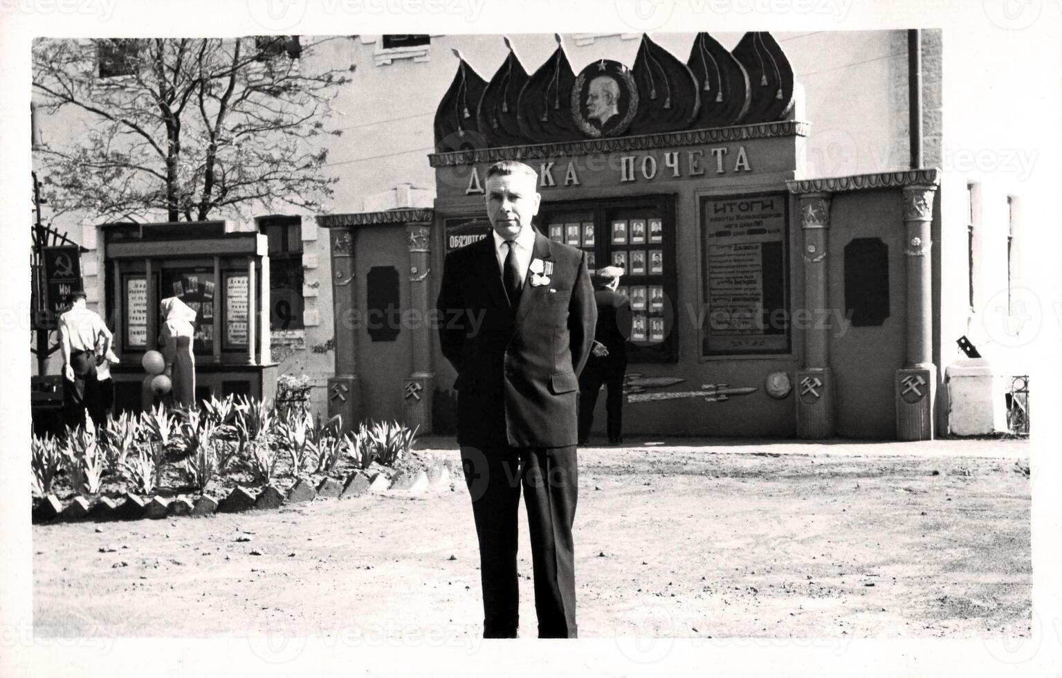Vintage portrait of an elderly man in the uniform of a USSR railway worker near the honor board. The inscription on the Russian Honor Board. photo