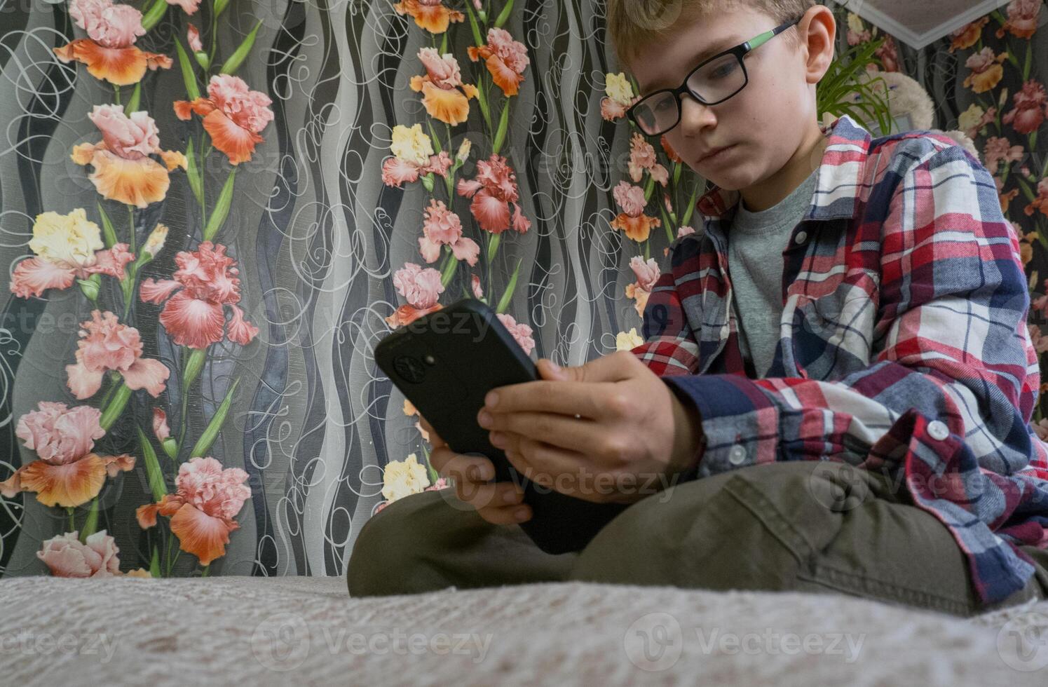A boy on the sofa with a mobile phone in his hands. The boy is addicted to gadgets and uses a mobile phone at home. Internet obsession concept photo