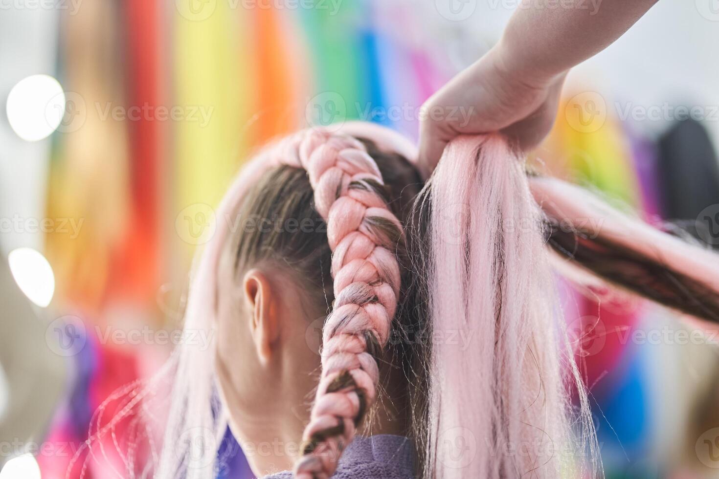 The master's hands weave kanekalon into the hair. A master braids pigtails for a child made of pink kanekalon. There is a place to copy photo