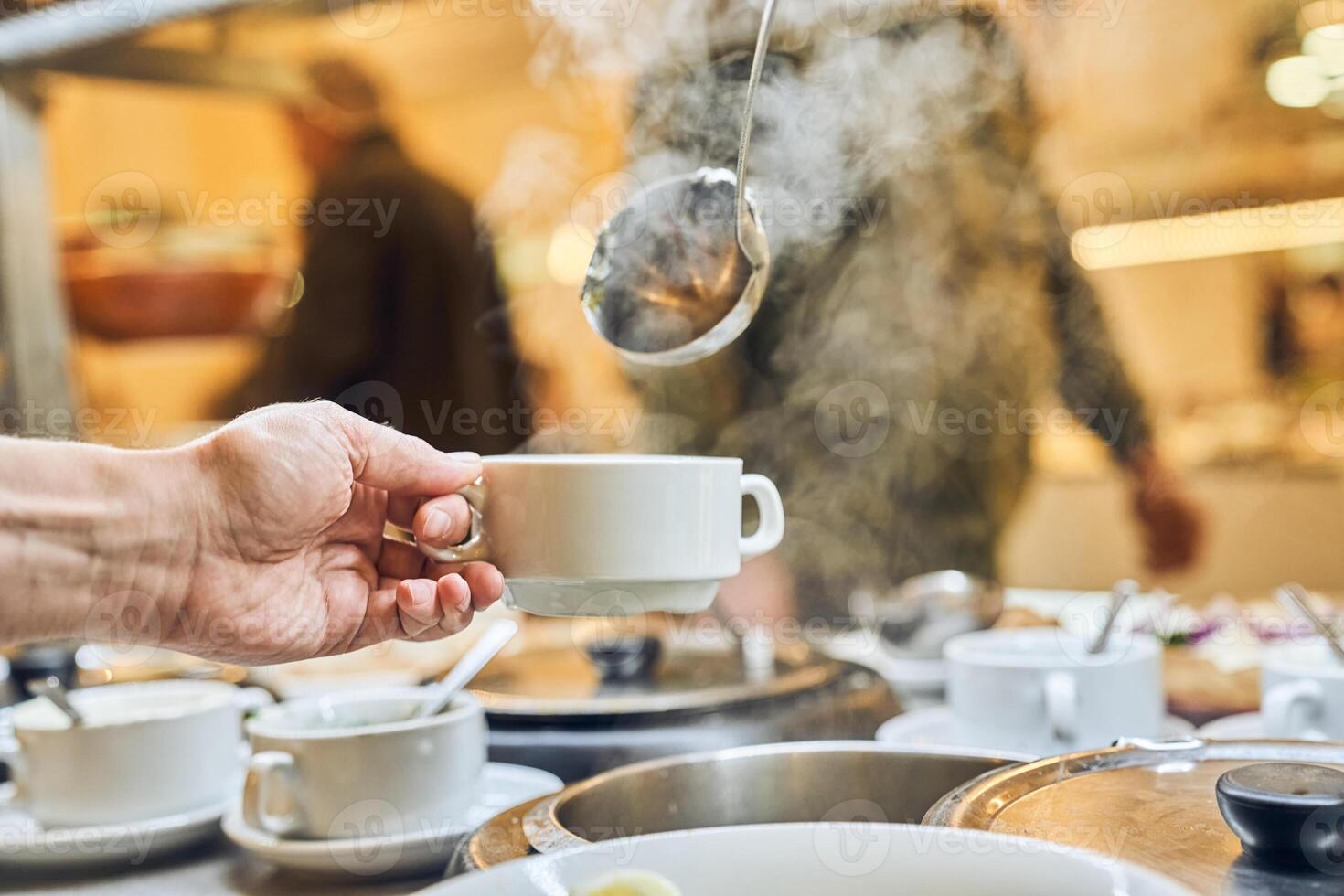Close-up of a hand against a background of steam pouring hot soup with a ladle. Free food in the charity canteen, with space for copying photo