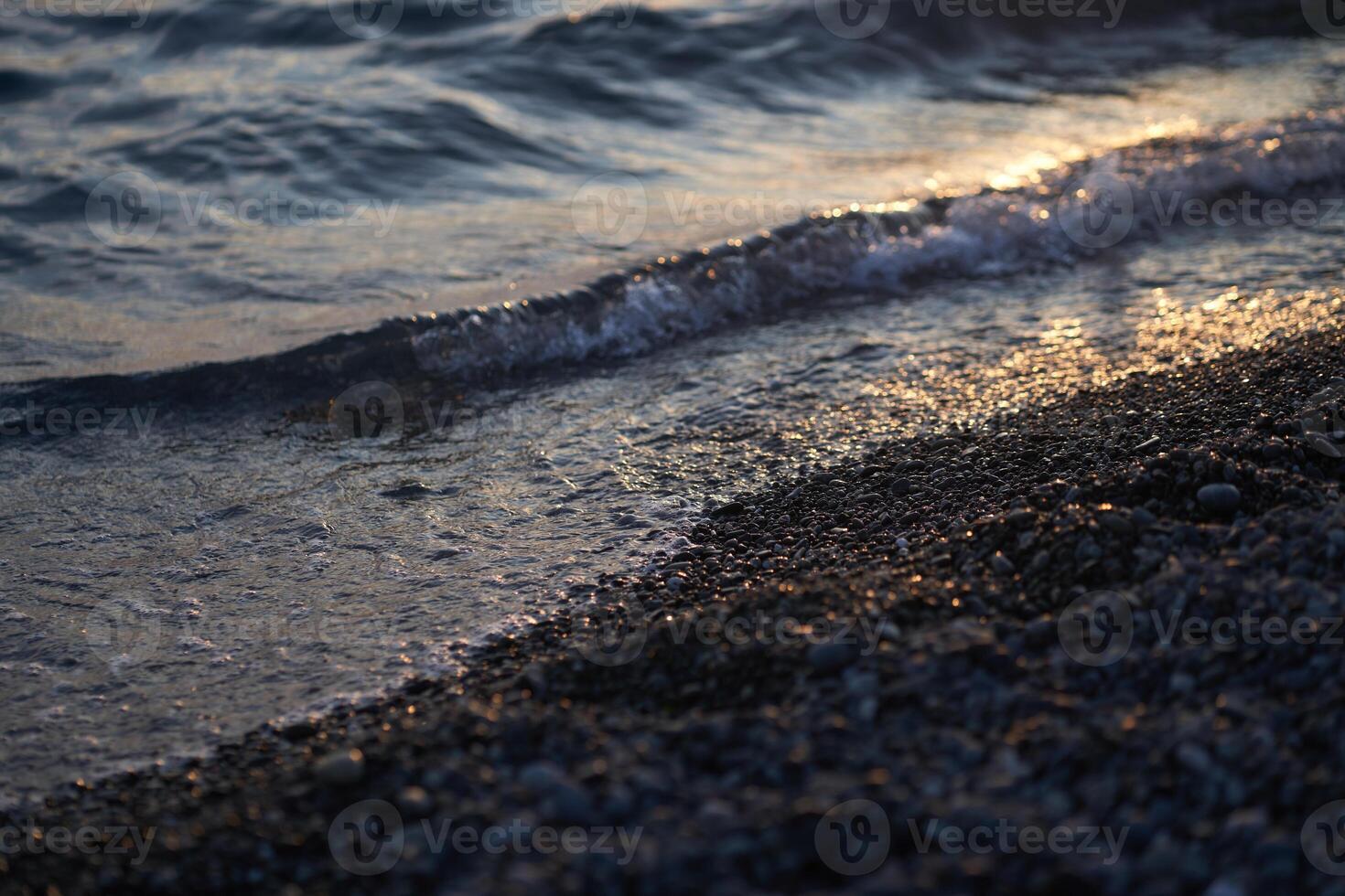 Water reaching the shore of a pebble beach in the afternoon sun. With space to copy photo