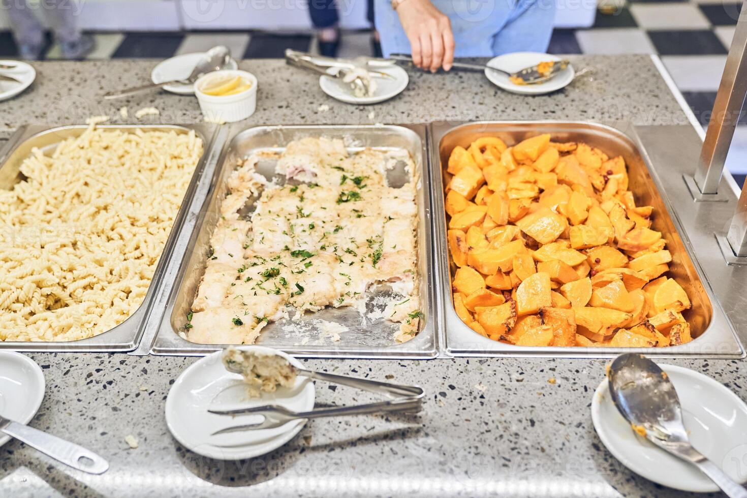 An unrecognizable volunteer putting food on plates in a charity canteen. A variety of nutritious hot food photo