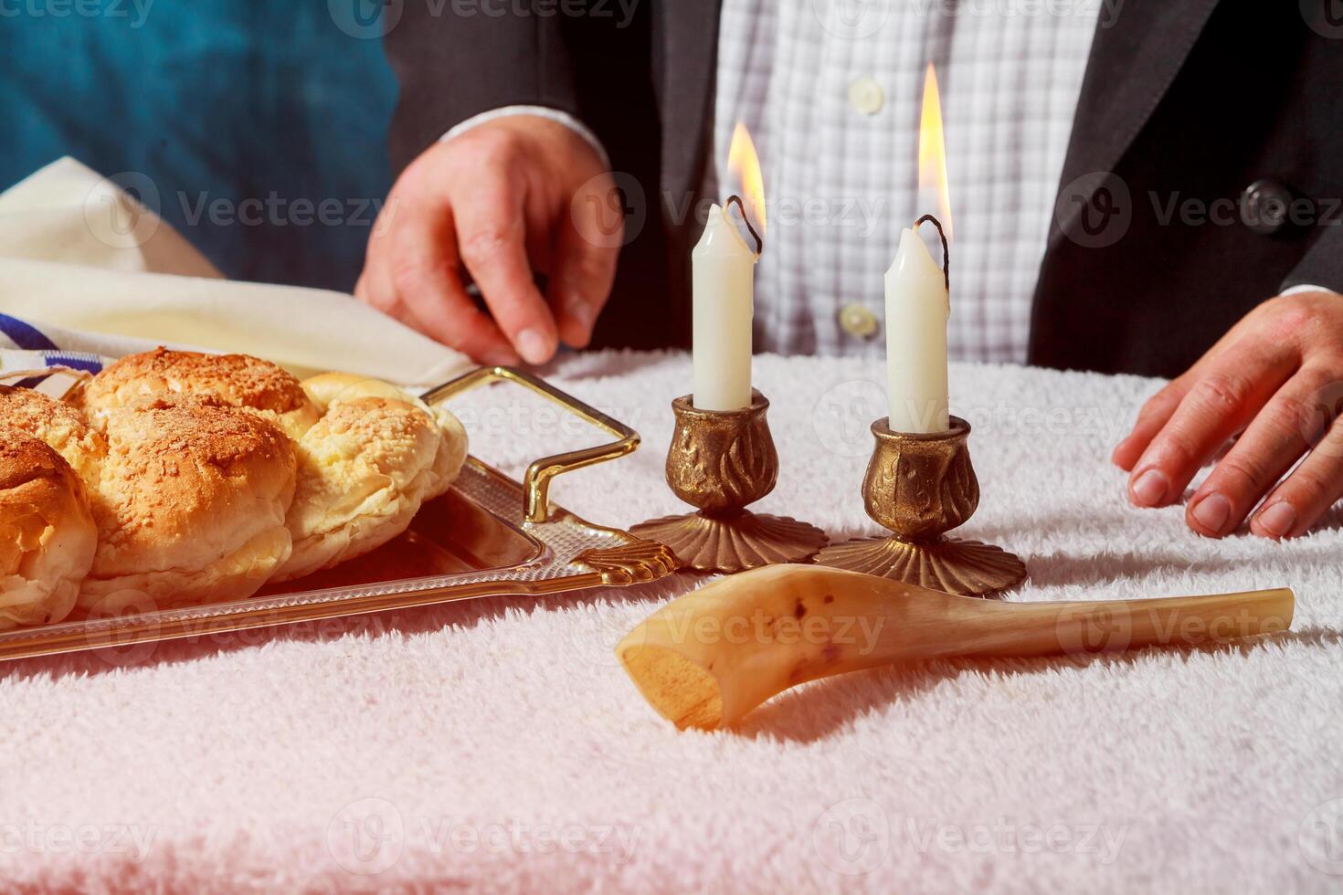 Challah or Hala is a traditional jewish sweet fresh sabbath bread loaf. Hands of men keep bread and two wax candles in candlesticks. photo