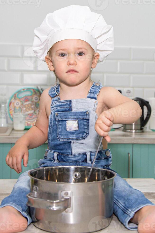 A young boy in overalls and a chef hat stirring a pot photo