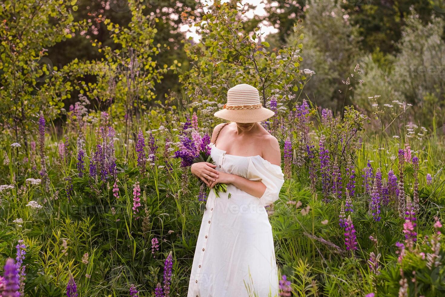A woman in a white dress and hat standing in a field of purple flowers photo