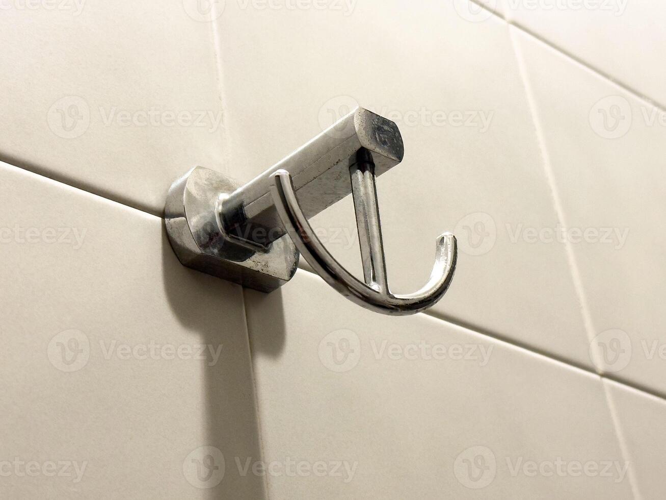 Metal wall-mounted towel hook on light tile bathroom wall photo