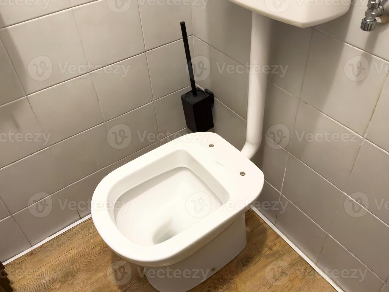 Clean white toilet in tiled bathroom with wooden floor and toilet brush photo