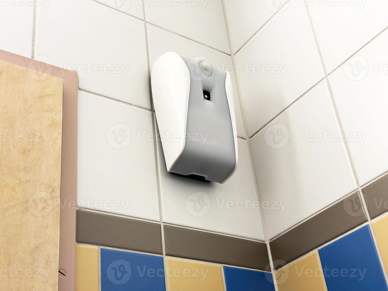 Wall-mounted automatic air freshener in tiled bathroom corner photo