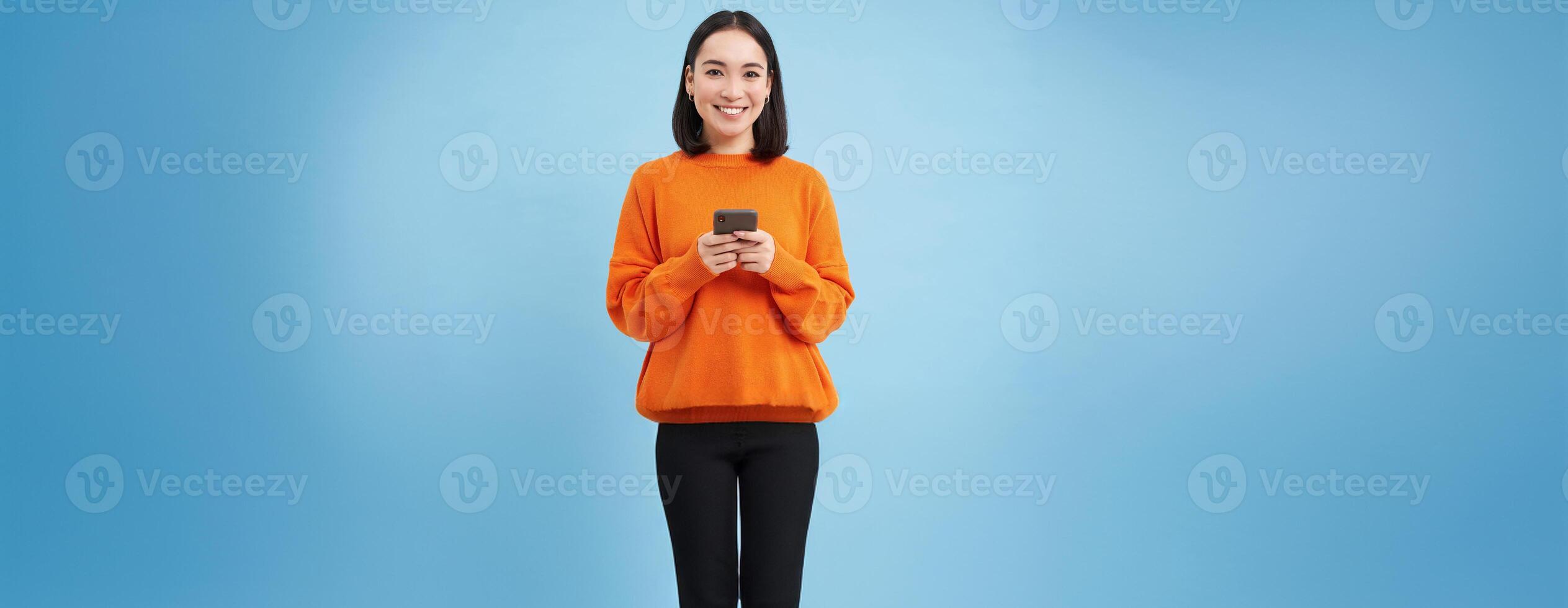 Girl with smartphone in hands smiling, using mobile application on her phone, sending message or order something online, blue background photo