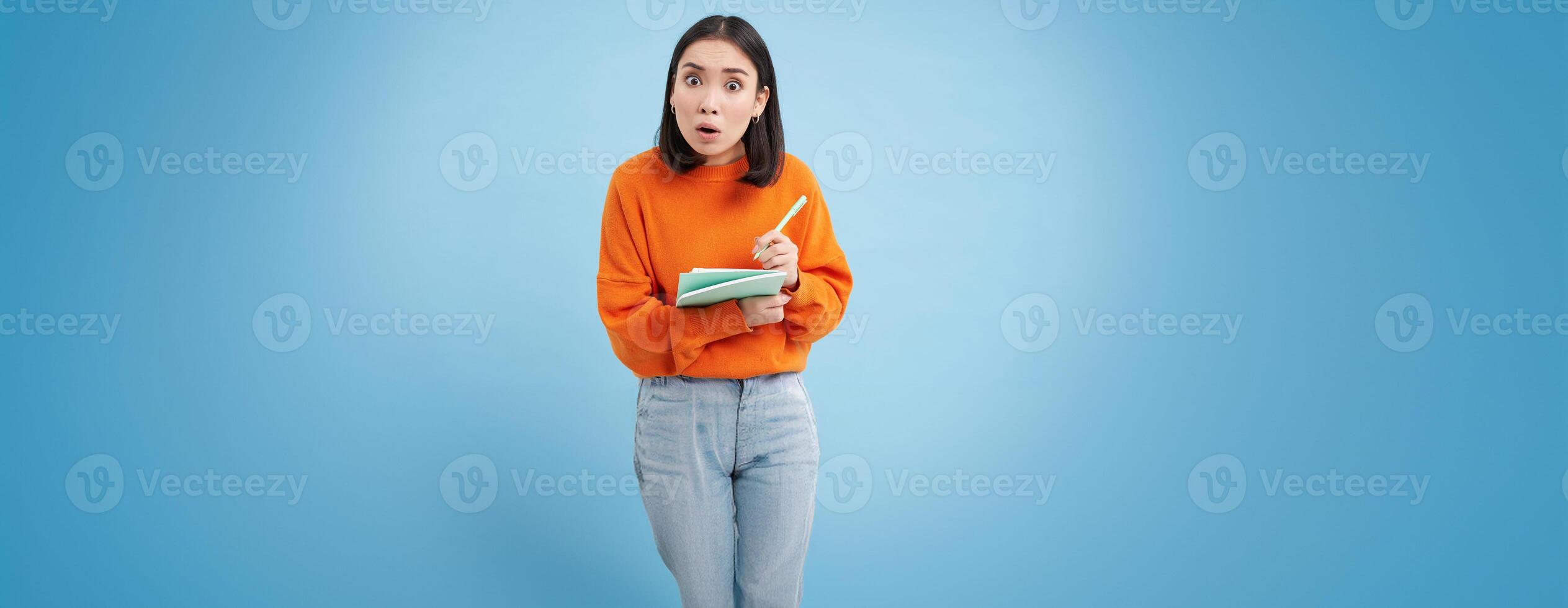 Education and students. Happy asian woman, holding notebooks and laughing, smiling at camera, enjoys going to University or College, blue background photo
