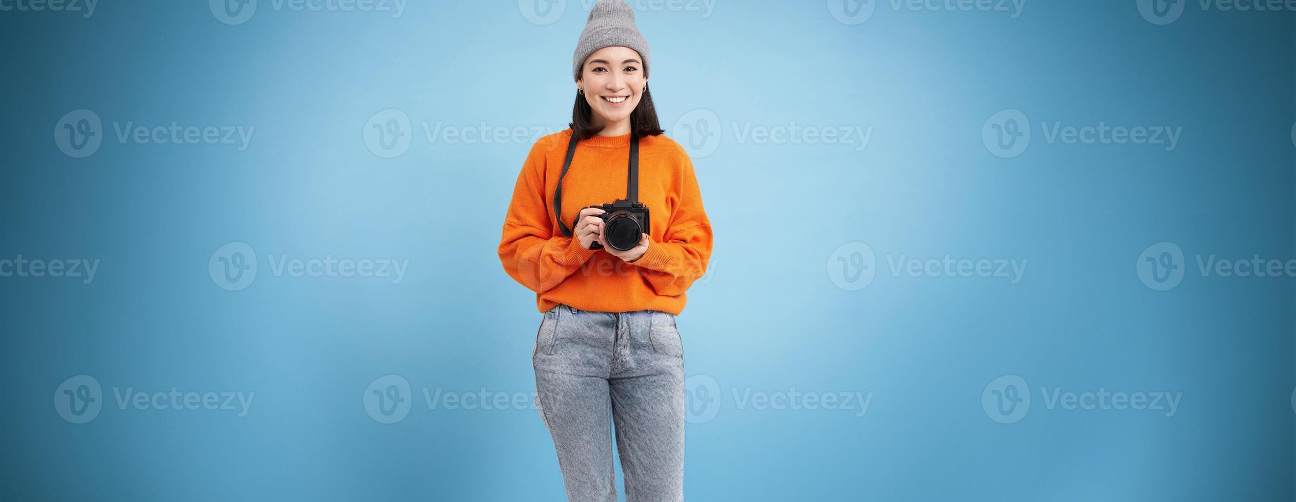 Stylish asian girl with digital camera, taking pictures. Woman photographer smiling, standing over blue background photo