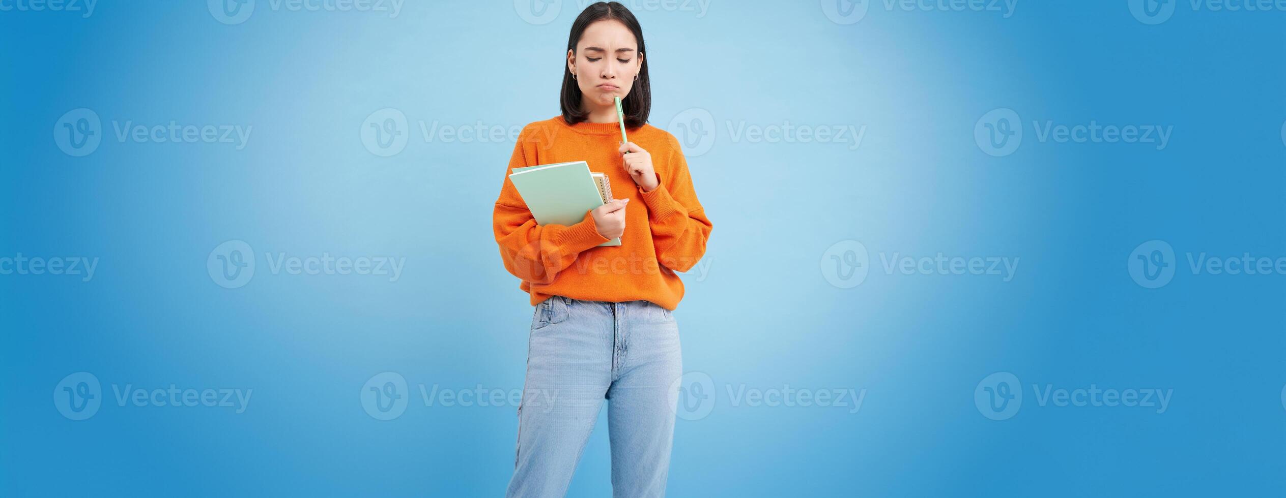 Education and students. Happy asian woman, holding notebooks and laughing, smiling at camera, enjoys going to University or College, blue background photo