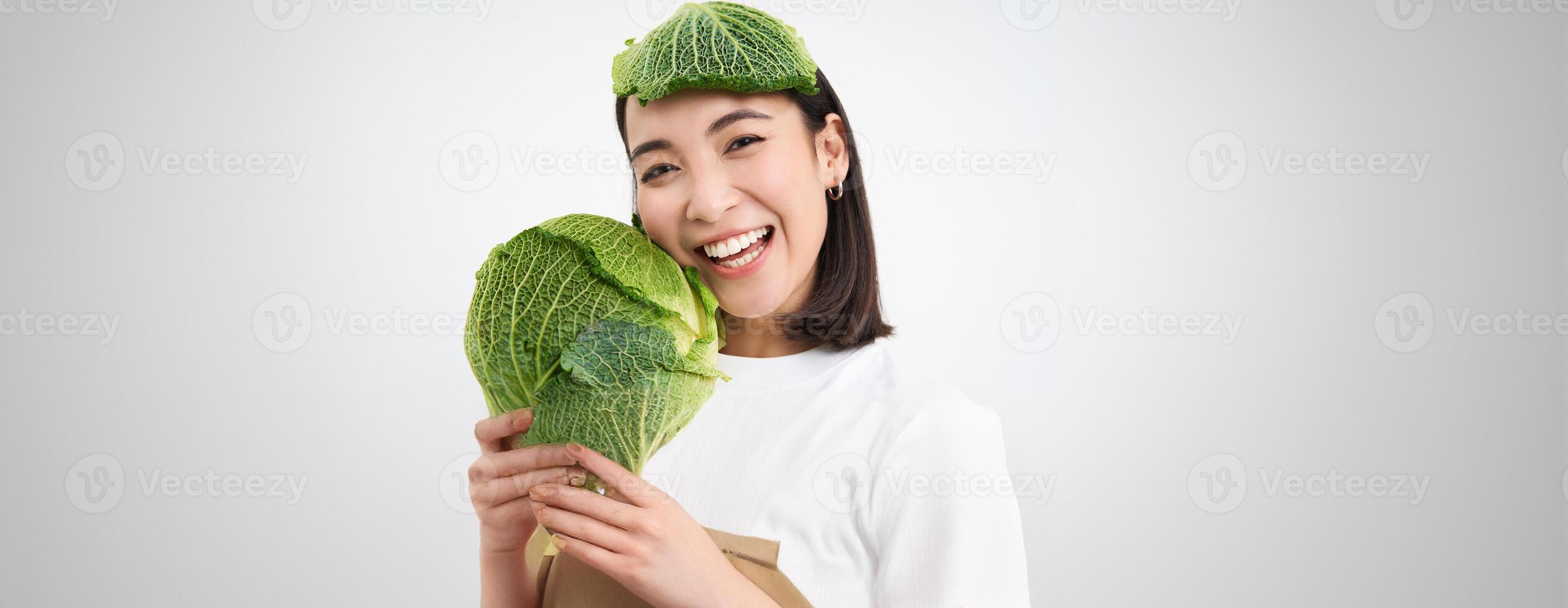 Close up portrait of healthy smiling asian woman, showing cabbage, green letture, with leaf on head, isolated on white background photo