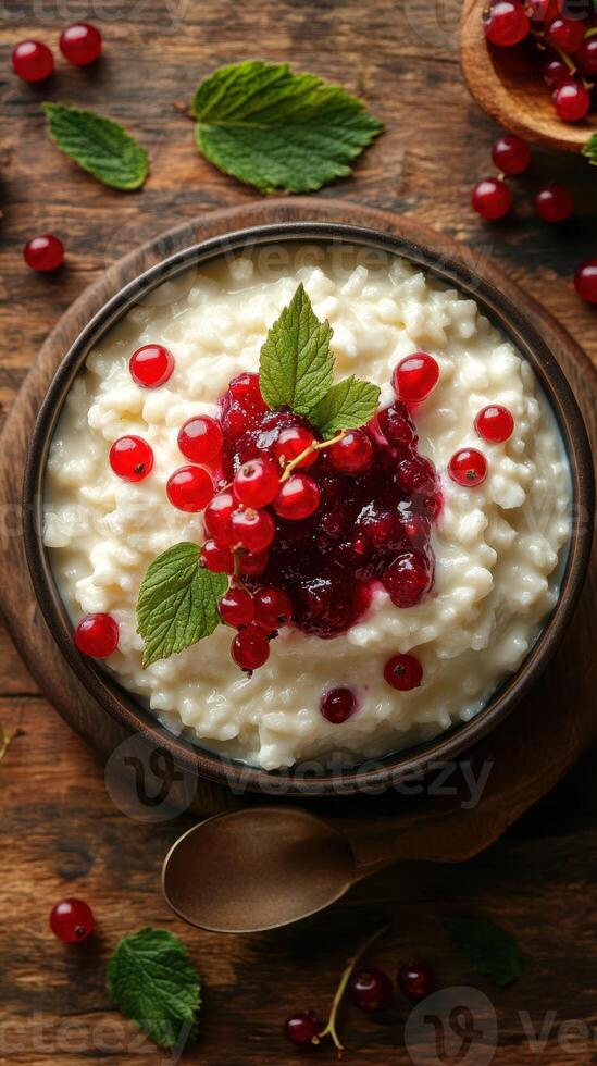 Creamy rice pudding topped with red currants and berry sauce on a rustic wooden table photo